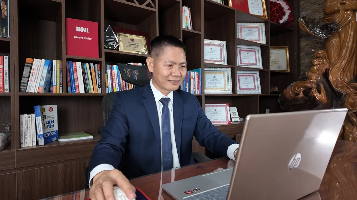 Anh Nguyễn Quốc Huy dùng laptop, kệ sách và giấy khen phía sau tại Tâm - Tầm - Tài – Chi phí thành lập công ty
