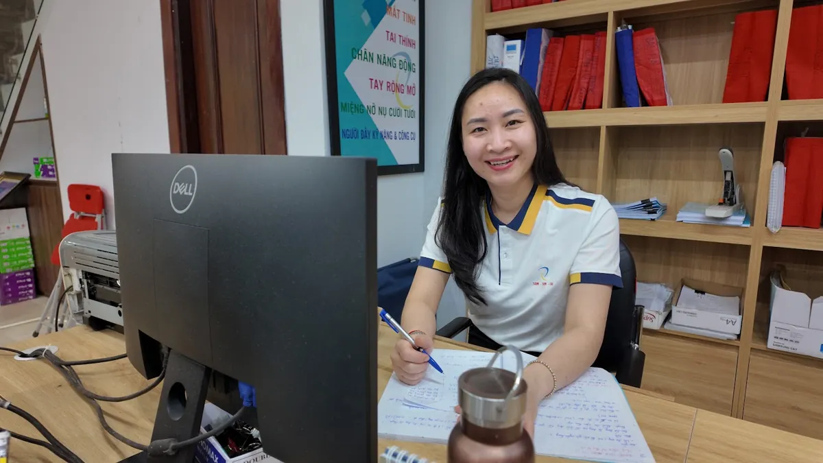 Nhân viên nữ đồng phục trắng ghi chép bên máy tính, mỉm cười tại Tâm - Tầm - Tài – Đăng ký kinh doanh ở đâu