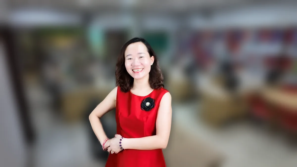 Chị Thảo Nguyễn váy đỏ chống hông, mỉm cười nhìn thẳng tại văn phòng Tâm - Tầm - Tài – chia sẻ về quy định dạy thêm học thêm